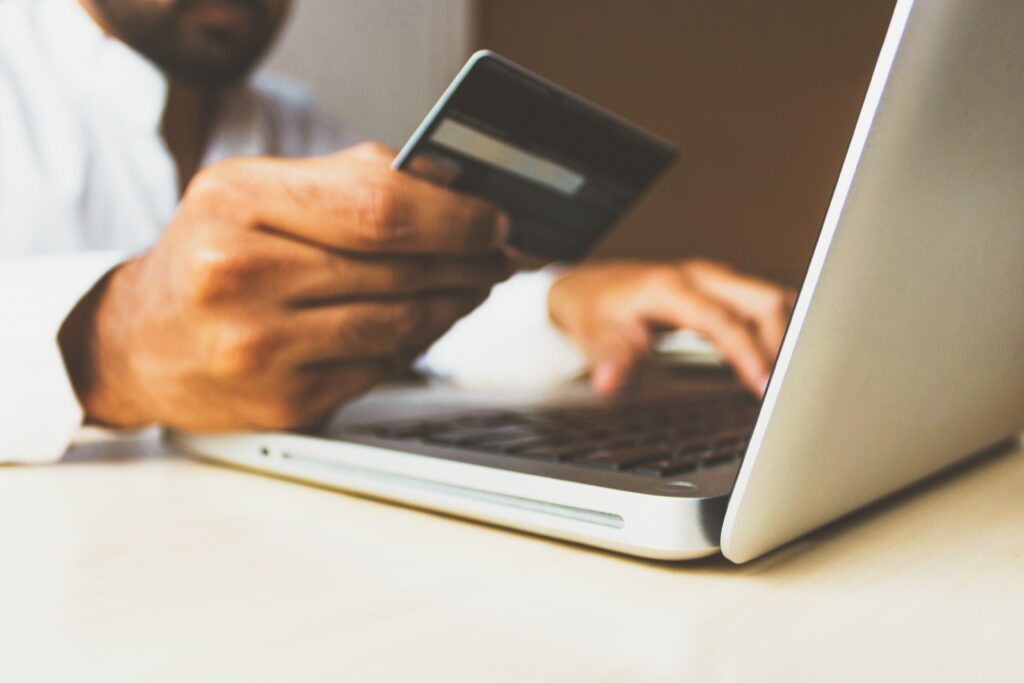 a man is shopping from an online store. one of his hands holds a credit card while the other hand is punching the credit card numbers into a computer. 